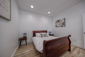 Een slaapkamer met een houten bed, een nachtkastje, een wandlamp en een lijst met een afbeelding.