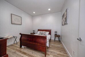 Een slaapkamer met een houten bed, een bureau, een stoel, een nachtkastje, een aan de muur hangend schilderij en een plafondlamp.