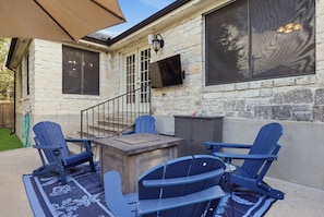Une terrasse avec un mur en pierre, un téléviseur fixé au mur et un espace extérieur aménagé avec des chaises et une table.
