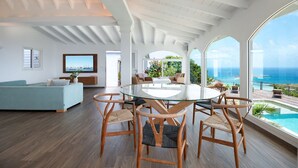 A spacious living area with a large glass table surrounded by chairs, a sofa, and a view of the ocean. - Villa Ocean Vibes (2 bedrooms) (San Bartolomé)