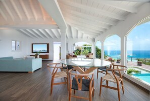 A spacious living area with a large glass table surrounded by chairs, a sofa, and a view of the ocean. - Villa Ocean Vibes (2 bedrooms) (San Bartolomé)