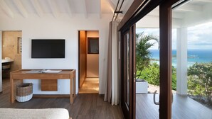 Ein modernes Hotelzimmer mit großem Fenster und Meerblick, einem Holztisch, einem Flachbildfernseher und einem gemütlichen Bett.