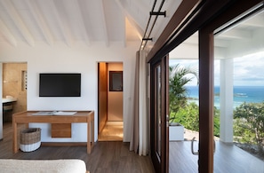 Ein modernes Hotelzimmer mit großem Fenster und Meerblick, einem Holztisch, einem Flachbildfernseher und einem gemütlichen Bett.