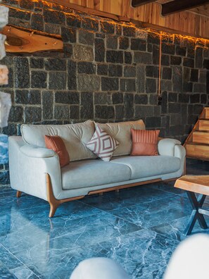 A modern living room with a stone wall, a light-colored sofa with cushions, and a wooden coffee table. - Kunç Konakları (Çamlıhemşin)