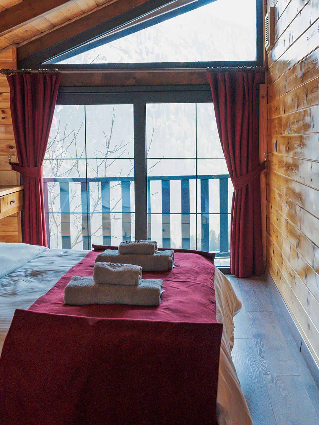 A room with a bed, a window with curtains, and a view of a balcony.