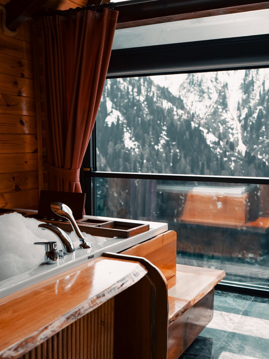 A wooden cabin interior with a window view of a forest and a sink with a wooden countertop.