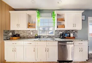 A kitchen with white cabinets, a stainless steel dishwasher, a window with a view, and a countertop with a coffee maker and toaster.
