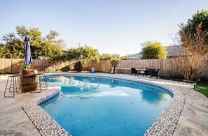En swimmingpool med en stenkant, et træhegn og udendørs møbler.