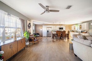 A modern living room with a sofa, dining table, chairs, and a kitchen area with cabinets and appliances.