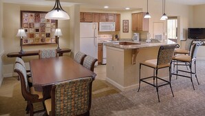 A spacious kitchen with wooden cabinets, a central island, and a dining area with a table and chairs. - Orlando | Pool & Disney Access | 2BR Suite (Lake Buena Vista)