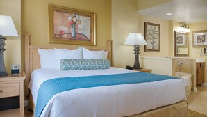A hotel room with a large bed, two bedside tables, a nightstand, a lamp, a painting, a mirror, and a bathroom with a bathtub and sink. - Orlando | Pool & Disney Access | 2BR Suite (Lake Buena Vista)