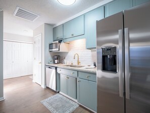 A modern kitchen with stainless steel appliances, light blue cabinets, and a white tiled backsplash.