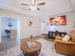 A modern living room with a fireplace, a ceiling fan, and a bar area.