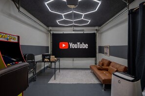 A room with a YouTube logo on the wall, a gaming console, a brown leather couch, and a speaker.