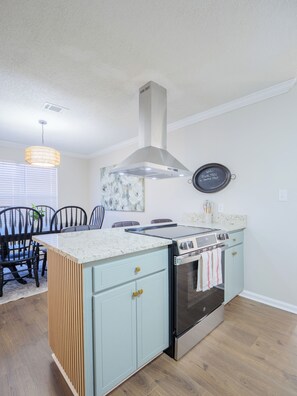 A kitchen with a central island, a stove, and a range hood. There is a dining area with chairs and a table. - Movie Theater, Arcade, Fire Pit, Cabana, Minutes from Freedom Park (Valdosta)