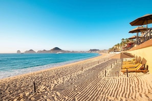 A beach with sun loungers and umbrellas, a clear blue sea, and distant mountains. - Beachfront 3BR Villa-Medano Beach, Cabo San Lucas (Cabo San Lucas)