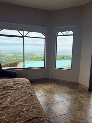 A bedroom with a large bed, two windows with a view of a landscape and a pool, and a tiled floor. - Fantastic 3-bedroom house in Playa Hermosa. Best views in of Playa Hermosa (Playa Hermosa)