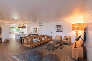Ein großzügiger Wohnbereich mit Sofa, Couchtisch und einer Essecke mit Hocker.
