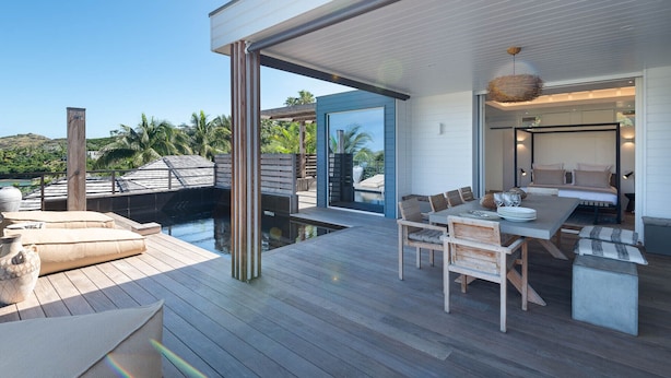 Una terraza moderna al aire libre con piscina, mobiliario de madera y vistas del paisaje circundante.
