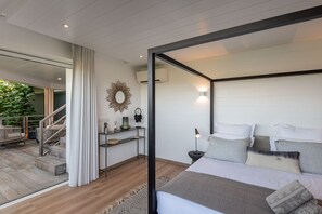 Ein modernes Schlafzimmer mit Bett, Nachttisch und Blick auf einen Balkon mit Pflanzen.