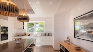 Una cocina moderna con una isla central, taburetes de bar, un amplio ventanal con vistas y una lámpara colgante.