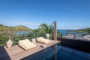 Ein Poolbereich mit Holzterrasse, Liegestühlen und Blick auf das Meer.