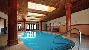 En indendørs swimmingpool med træbjælker og -søjler, glasdøre og flisegulv.