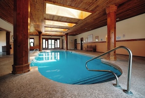Una piscina interior con vigas y columnas de madera, puertas de vidrio transparente y suelo de baldosas.