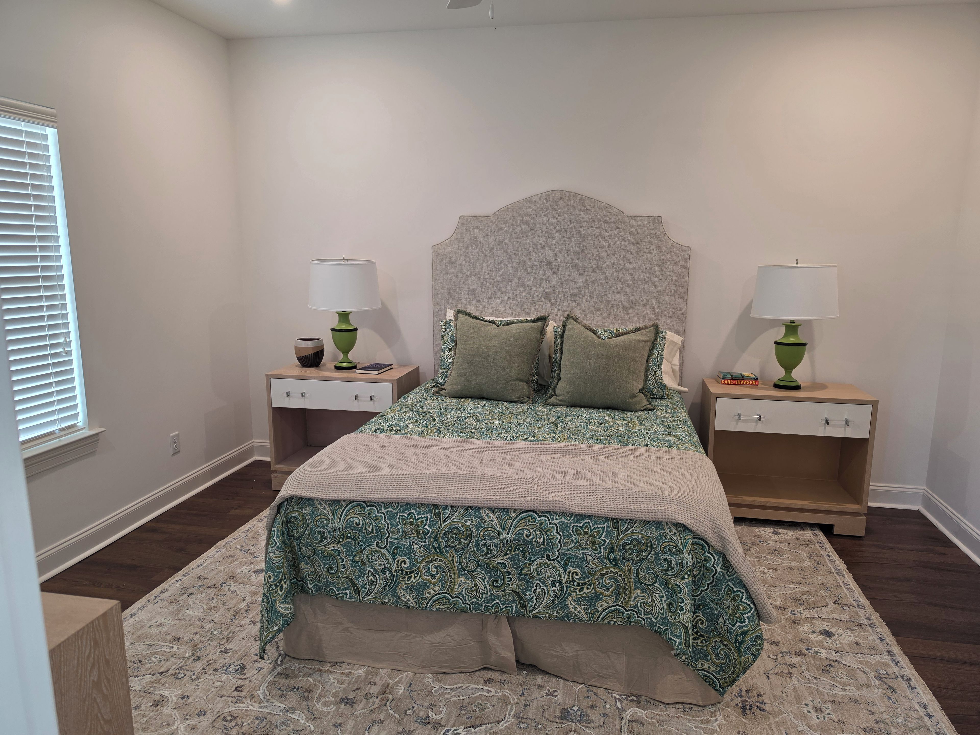 A bedroom with a bed, two nightstands, a headboard, and a window with blinds.