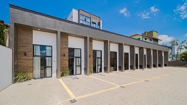A modern building with multiple entry points, a paved parking area, and a clear sky.