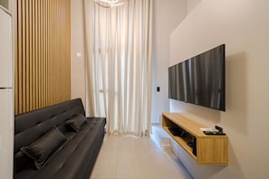 A modern living room with a black sofa, a wooden accent wall, a TV mounted on the wall, and a white curtain. - Garten - Studios mordenos (Joinville)