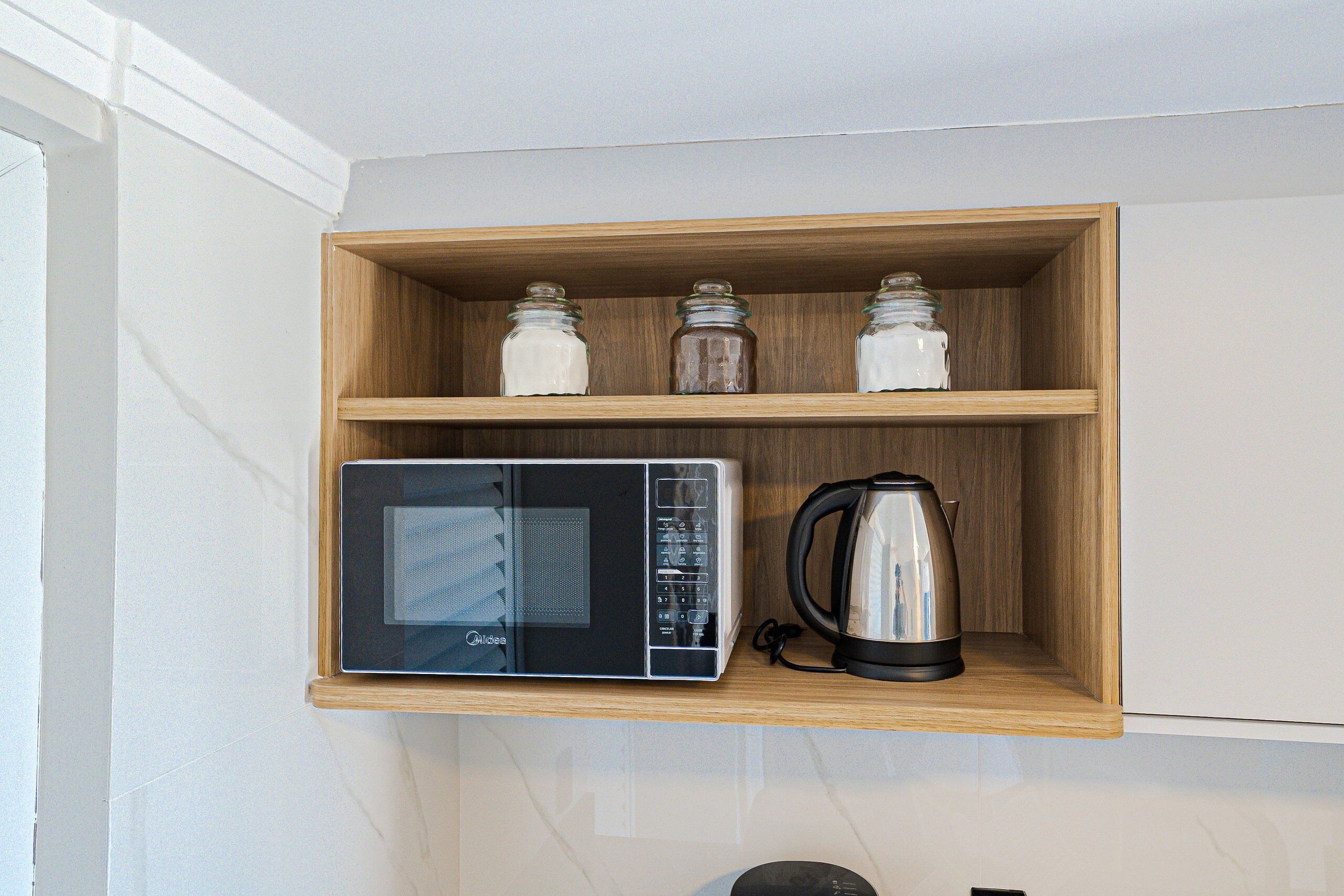 A kitchen with a microwave on a wooden shelf, a kettle, and three glass jars.
