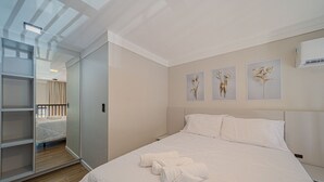 A neatly made bed with white linens and towels, a bedside table, and a wall with three framed floral artworks.