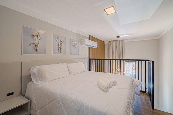A neatly made bed with white linens, a bedside table, and three wall-mounted floral art pieces.