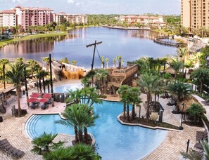 A resort with a central pool, palm trees, and a water body. - Orlando | Pool & Disney Access | Theme Park Getaway (Lake Buena Vista)
