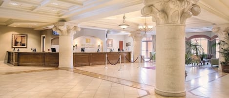 Un hall d’entrée spacieux avec un comptoir d’accueil, des colonnes et un lustre.