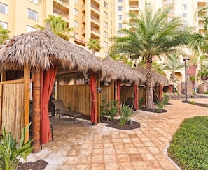 Ein Resort mit strohgedeckten Cabanas, Liegestühlen und einem gepflasterten Weg.