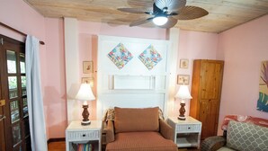A cozy room with a bed, two nightstands with lamps, a patterned ottoman, a wooden cabinet, and a door with a glass panel. - Papaya Place Divers Inn, a comfortable quite place fabulous West Bay. (West Bay)