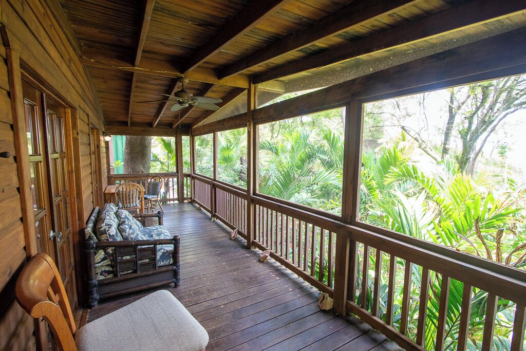 A wooden deck with a sofa and chairs, overlooking lush greenery.