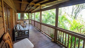 A wooden deck with a sofa and chairs, overlooking lush greenery. - Papaya Place Divers Inn, a comfortable quite place fabulous West Bay. (West Bay)