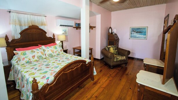 A bedroom with a wooden bed, a ceiling fan, a chair, and a painting on the wall. - Papaya Place Divers Inn, a comfortable quite place fabulous West Bay. (West Bay)