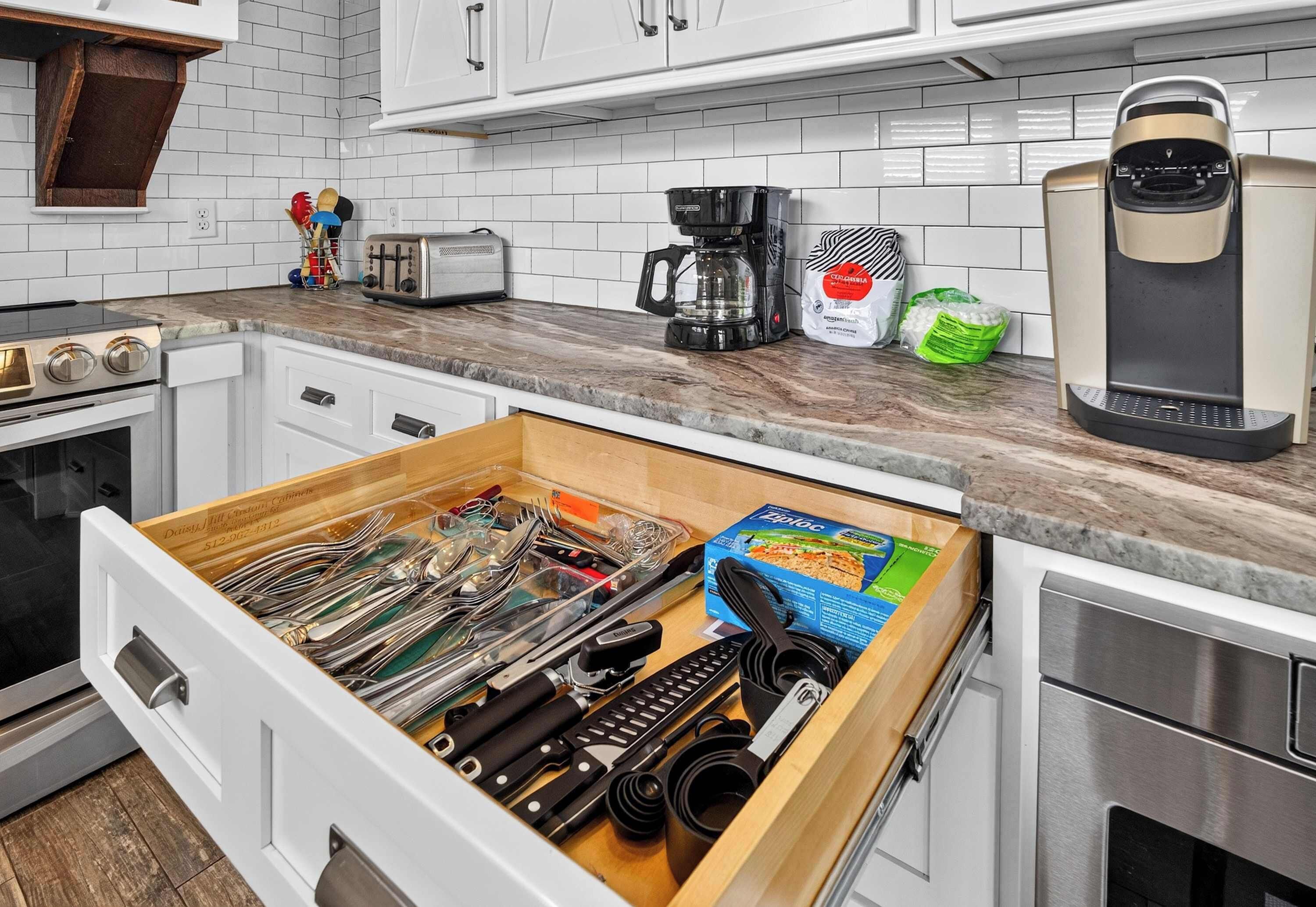 A kitchen with white cabinets, a drawer organizer with utensils, a coffee maker, and a toaster.