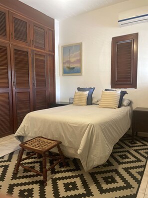 A bedroom with a bed, a wooden wardrobe, a painting, and a patterned rug. - Artistic & Comfortable 2BR Apartment in Bella Vista (Santo Domingo)