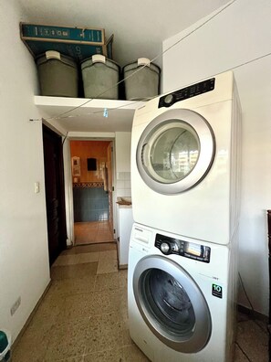 Een wasserette met gestapelde wasmachines en drogers, een betegelde vloer en een deur naar een keuken.