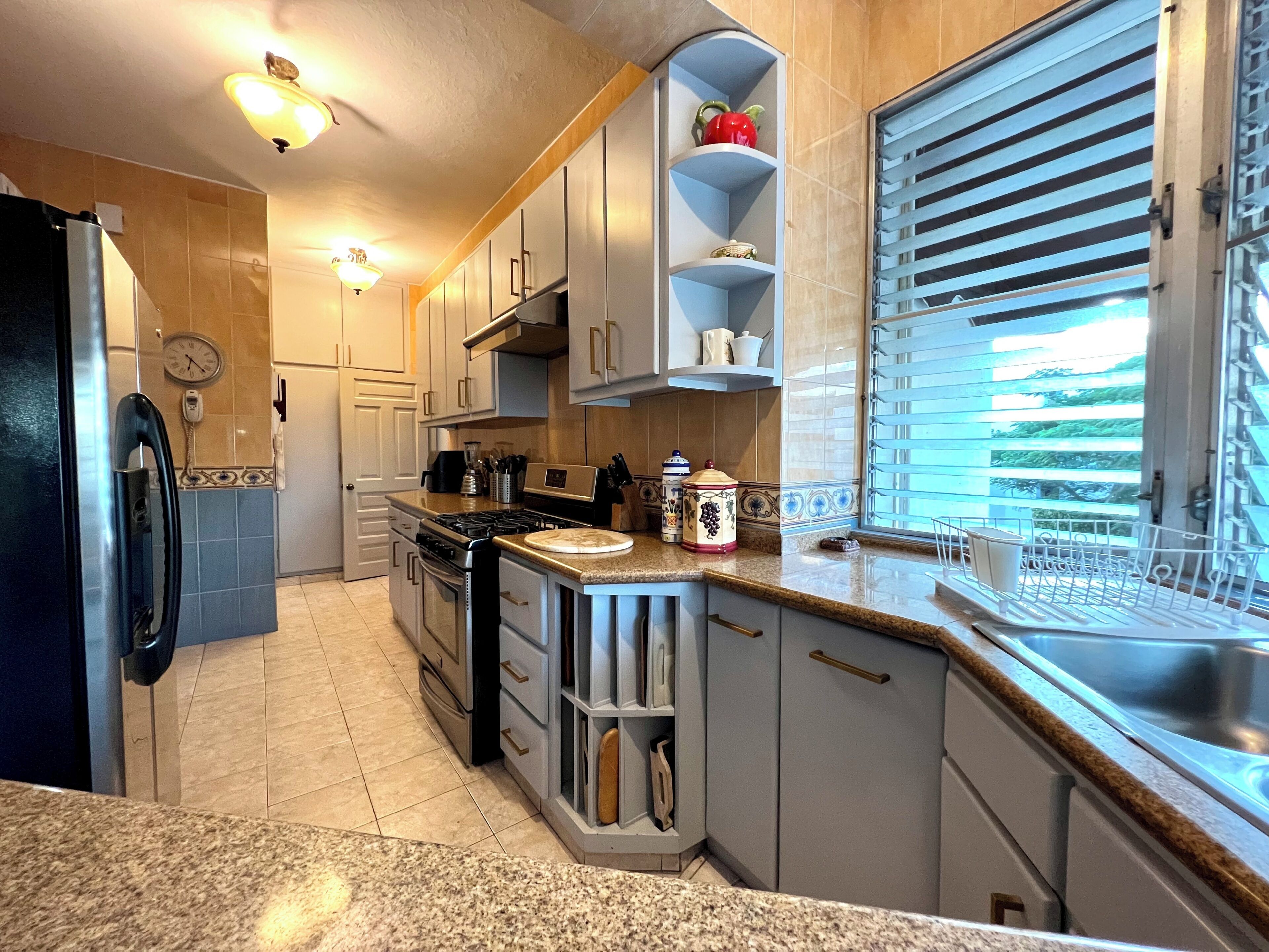 Una cocina con estufa, horno y refrigerador. Tiene una ventana con persianas y un lavamanos.