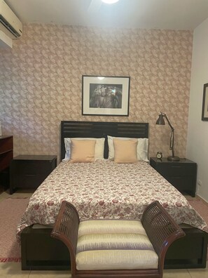 Een slaapkamer met een bed, twee nachtkastjes, een bureau, een stoel en een lijst aan de muur.