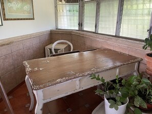 A corner room with a wooden table, a white chair, a window with blinds, and a potted plant. - Artistic & Comfortable 2BR Apartment in Bella Vista (Santo Domingo)