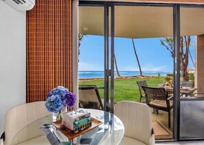 A room with a glass table, chairs, a vase of flowers, and a view of the ocean. - Valley Isle Villas | Oceanfront Studio Sleeps 4 | Car Incl. w/ 6+ Nights | VIR-107 by KBM (Lahaina)