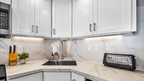 Una cocina moderna con armarios blancos, horno empotrado, tostadora y encimera de mármol.