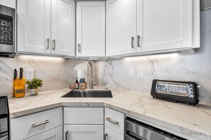 A modern kitchen with white cabinets, a built-in oven, a toaster, and a marble countertop. - Valley Isle Villas | Oceanfront Studio Sleeps 4 | Car Incl. w/ 6+ Nights | VIR-107 by KBM (Lahaina)